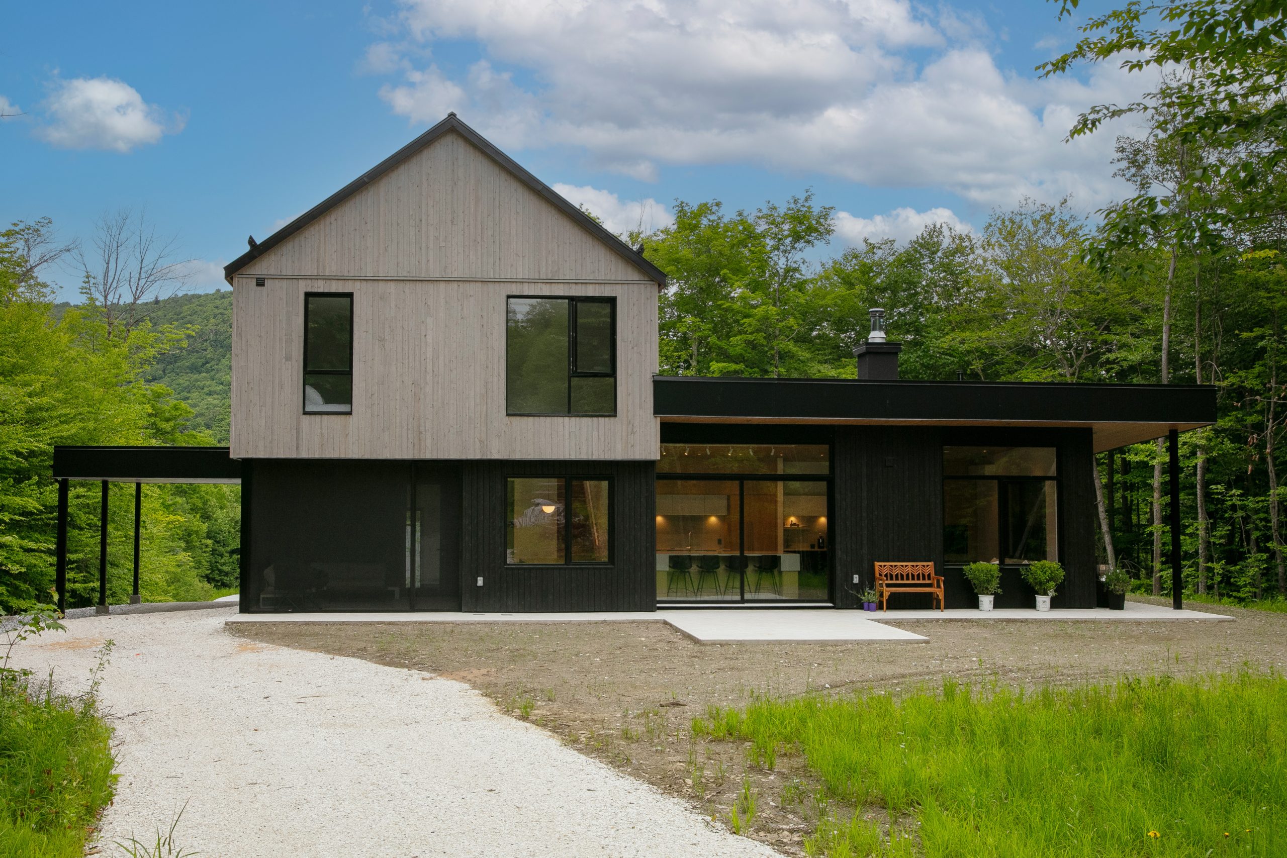 Volumes scandinaves de la Résidence G + R construite par Structures RP3 avec fenestration noire contrastée et revêtement gris pâle, en pleine forêt.